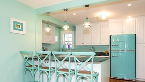 Une cuisine avec des chaises et un réfrigérateur de couleur turquoise, ainsi que des luminaires suspendus.