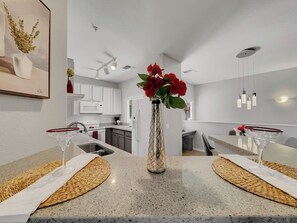 A modern kitchen with white cabinets, a stainless steel sink, and a dining area with a granite countertop and woven placemats. - Superstition Springs Mesa (Mesa)