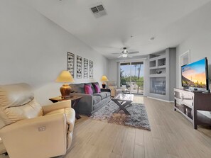 A modern living room with a sofa, two armchairs, a coffee table, and a TV. There are ceiling fans, a fireplace, and a balcony with a view. - Superstition Springs Mesa (Mesa)