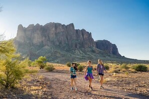 Three people walking on a rocky path with a large rock formation in the background. - Superstition Springs Mesa (Mesa)