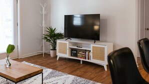 A living room with a flat-screen TV on a white cabinet, a potted plant, and a coffee table with a vase. - The Cozy Corner Near Downtown (Athens)