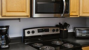 A kitchen with wooden cabinets, a stainless steel microwave, a gas stove, and a built-in oven. - The Cozy Corner Near Downtown (Athens)