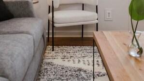 A room with a grey sofa, a white chair, a wooden table, and a patterned rug. - The Cozy Corner Near Downtown (Athens)