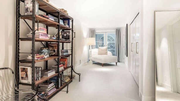 A hallway with a bookshelf, a white armchair, and a door. - Bull Path Manor by Rove - 4BR Family Home With Pool & Hot Tub (East Hampton)
