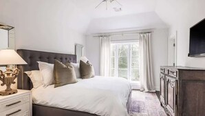 A bedroom with a large bed, a nightstand, a dresser, a ceiling fan, and a window with curtains. - Bull Path Manor by Rove - 4BR Family Home With Pool & Hot Tub (East Hampton)