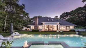 A house with a swimming pool, surrounded by trees and a well-maintained lawn. - Bull Path Manor by Rove - 4BR Family Home With Pool & Hot Tub (East Hampton)