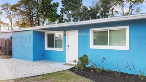 Una casa de un piso con fachada azul, una puerta blanca y dos ventanas con marcos blancos.