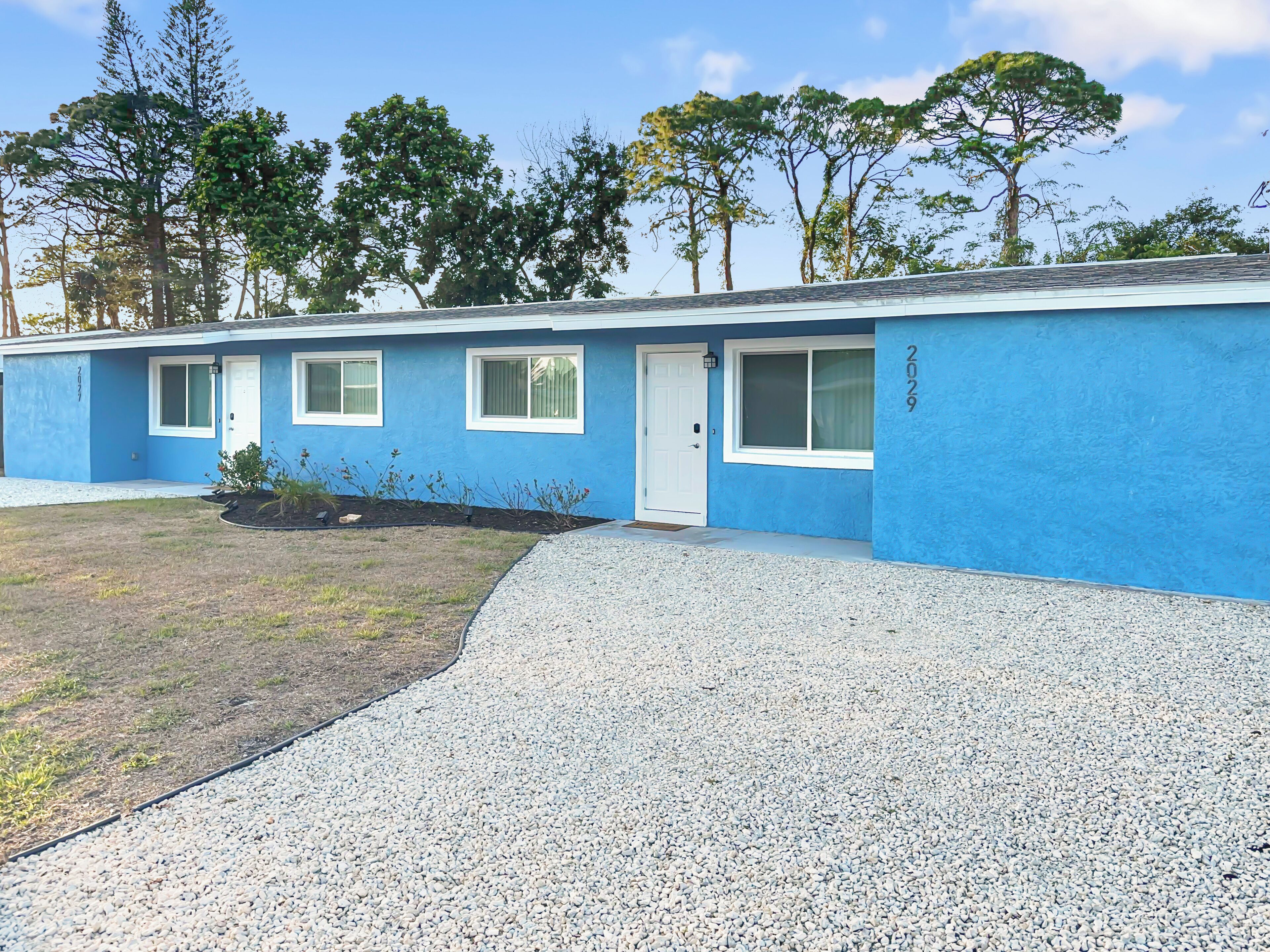 Un motel de un piso con fachada azul, detalles blancos y entrada de grava.