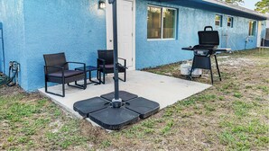 Una casa azul con un patio que tiene mobiliario exterior, una parrilla y una zona de estar cubierta.