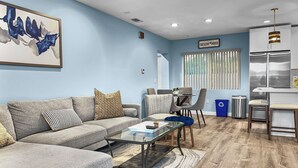 Una sala de estar moderna con un sofá seccional gris, una mesa de centro de vidrio y un comedor con una pequeña mesa y sillas.