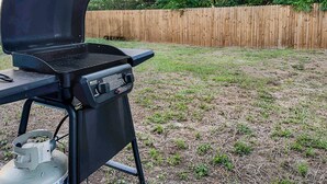 Ein Garten mit einem schwarzen Grill, einem Gasbehälter und einem Holzzaun.