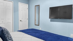 Ein Schlafzimmer mit einem Bett, einer weißen Tür, einem Spiegel und einem Fernseher an der Wand.