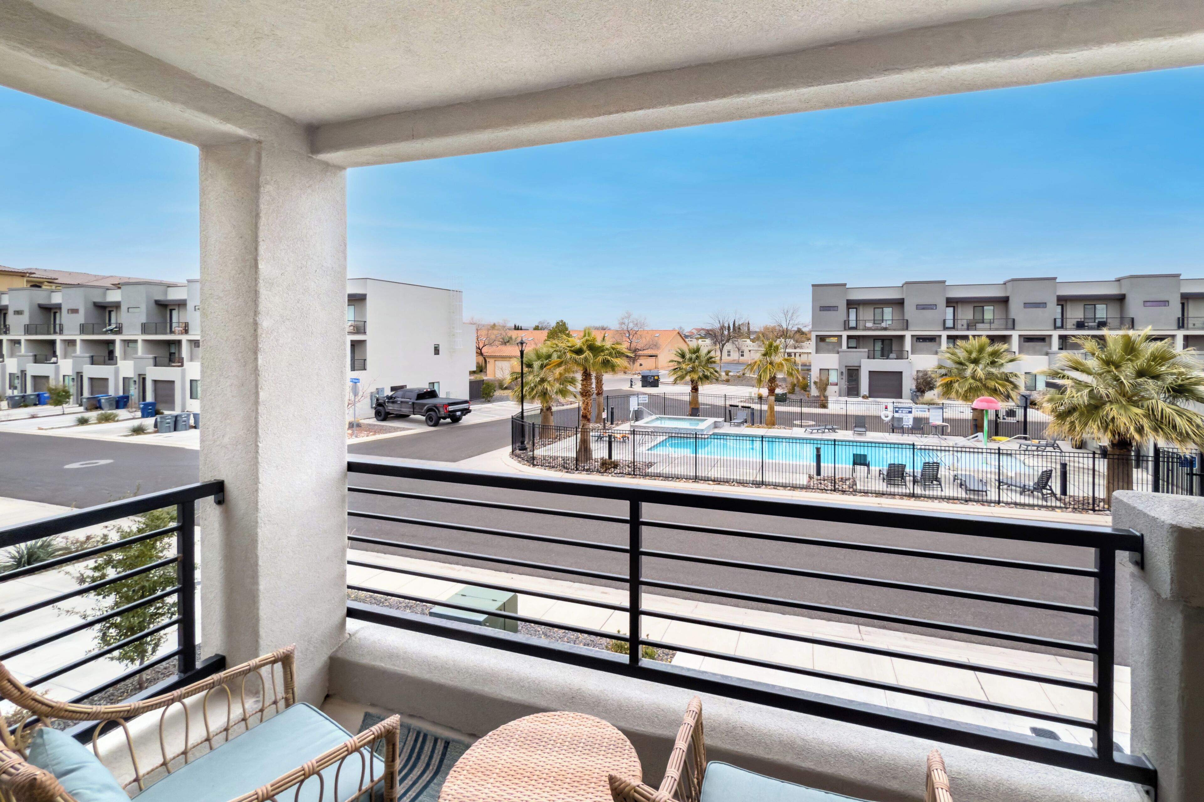 Ein Balkon mit Korbmöbeln, ein Pool und moderne Gebäude im Hintergrund.