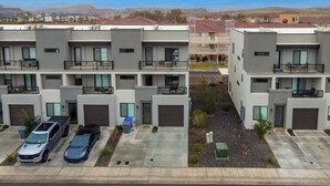 Un edificio residencial moderno de varios pisos con estacionamiento, dos automóviles y una vista despejada del paisaje circundante.