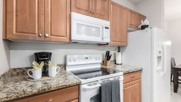A kitchen with wooden cabinets, a white microwave, a white stove, and a refrigerator.