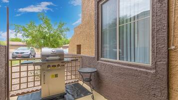 A patio with a grill, a small table, and a window overlooking a street.