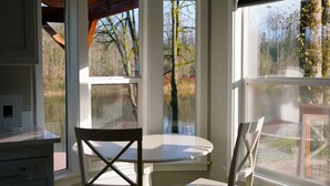 A corner room with a white table and two chairs, large windows with a view of trees and a garden. - Skyriver Escape Riverfront With Hot Tub (Monroe)
