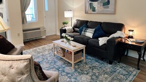 Un salon avec un canapé en cuir noir, une table basse en bois, un tapis à motifs bleus, une lampe et un tableau accroché au mur.