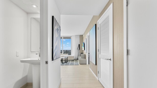 A modern hallway with a white sink, a sofa, and a view to a balcony. - Stunning High-floor City View 1BR Hyde Beach House (Hollywood)