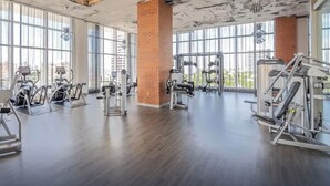 A spacious gym with various exercise equipment, large windows, and a brick column. - Stunning High-floor City View 1BR Hyde Beach House (Hollywood)