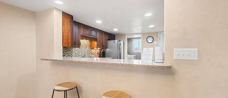 A modern kitchen with a central island, wooden bar stools, and built-in appliances.