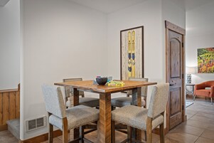 Uma sala de jantar com uma mesa de madeira e quatro cadeiras estofadas, um quadro na parede e uma porta com moldura de madeira.