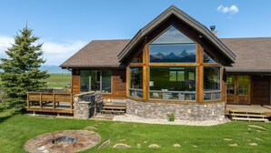 A log cabin with a stone foundation, large windows, and a deck. - Teton Melody (Driggs)