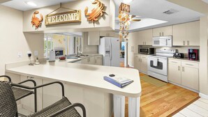 Een moderne keuken met een centraal eiland, witte kasten en een 'WELCOME' bord.