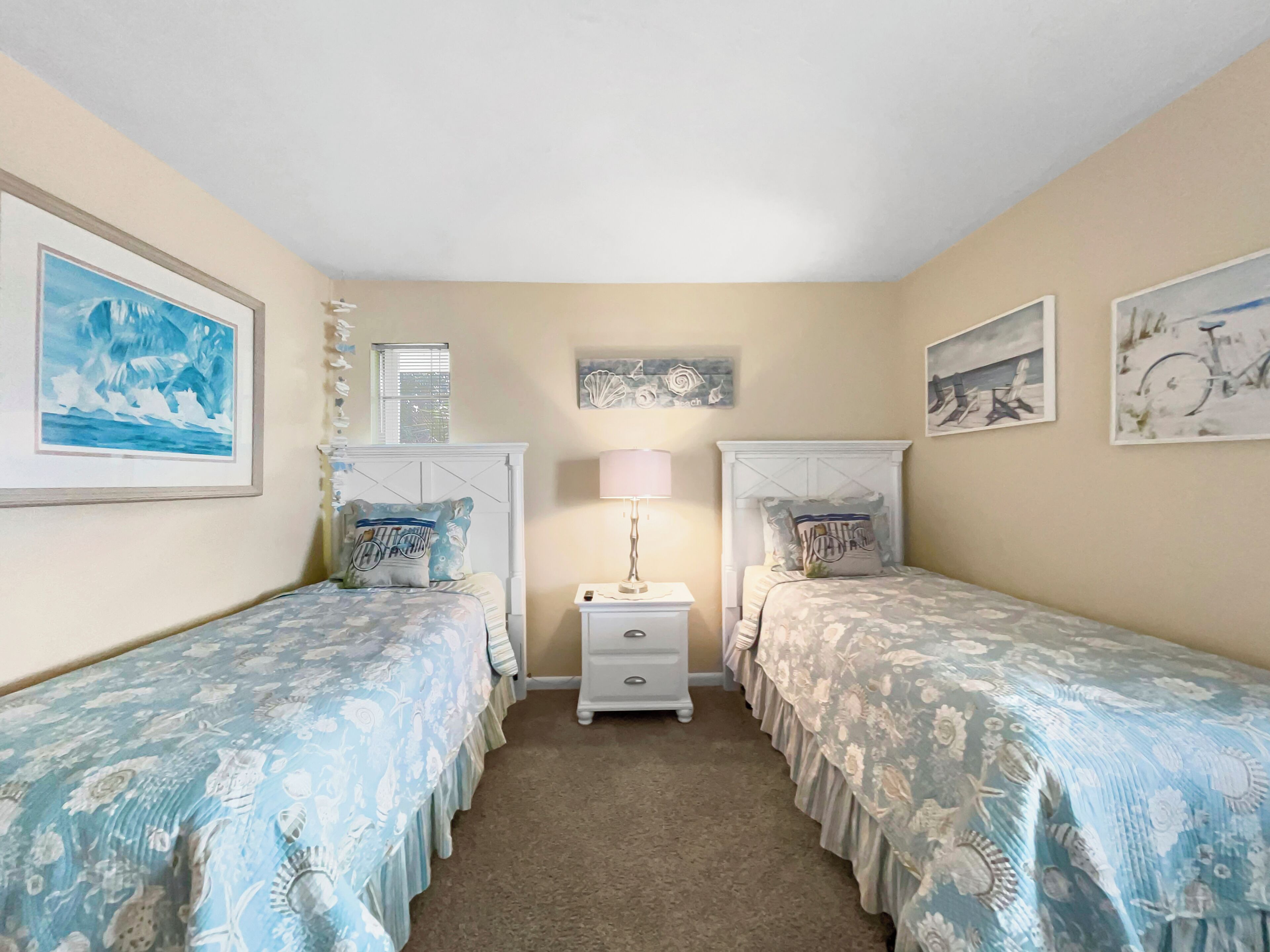 A bedroom with two single beds, a nightstand with a lamp, and wall art.