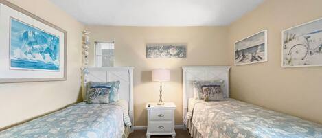 A bedroom with two single beds, a nightstand with a lamp, and wall art.