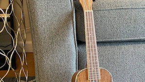 Un ukulele su un tappeto decorato, vicino a un divano grigio e un tavolino con struttura dorata.