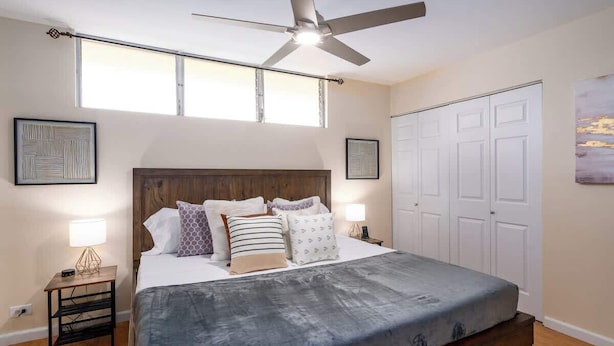 Una camera da letto con un letto, una ventola a soffitto, una finestra, una porta e un comodino con una lampada.