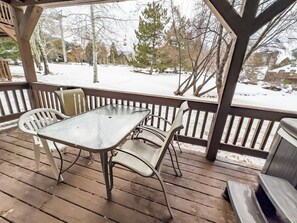 A covered outdoor area with a table and chairs, wooden flooring, and a view of a snowy landscape with trees and buildings. - Hidden Creek Pond View Perfection Canyons Parkcity (Park City)