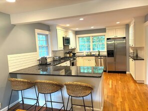 A modern kitchen with a central island, bar stools, stainless steel appliances, and large windows. - Haven on Glynn by Rove Travel - Coastal Luxury (Shelter Island)