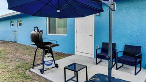 A patio with a grill, chairs, and a large umbrella. - Blue Haven A (Sarasota)