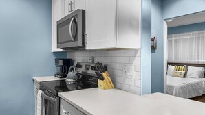 A modern kitchen with white cabinets, a built-in microwave, a kettle, and a coffee maker. - Blue Haven A (Sarasota)