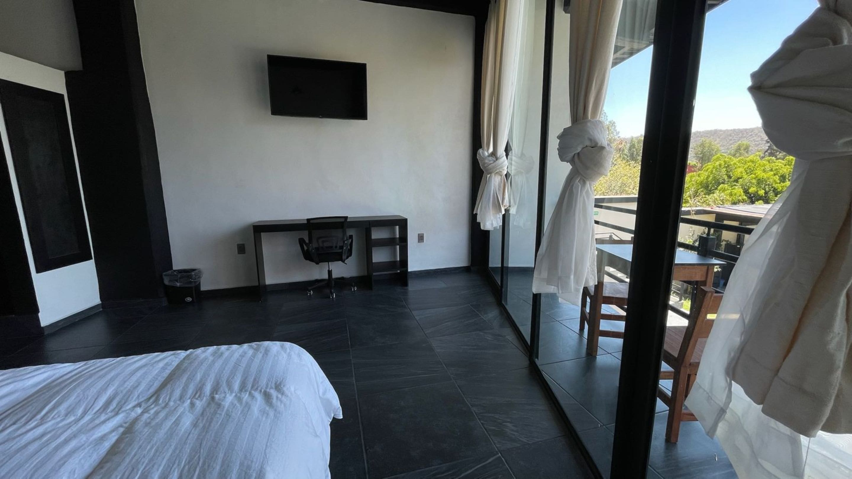 A modern hotel room with a bed, a desk, and a view of the outdoors.
