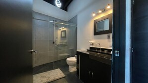 A modern bathroom with a glass shower enclosure, a toilet, and a sink with a mirror above it. - Villa DPJ el Arco (Valle de Bravo)