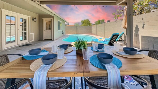 An outdoor patio with a pool, dining table set with bowls and glasses, and lounge chairs. - Yorkshire Glendale (Glendale)