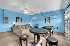 A room with a blue wall, a ceiling fan, a sofa, a coffee table, two bar stools, a television, and a foosball table. - Windsor Palms Resort 4 Bedroom With Game Room 0878 (Kissimmee)