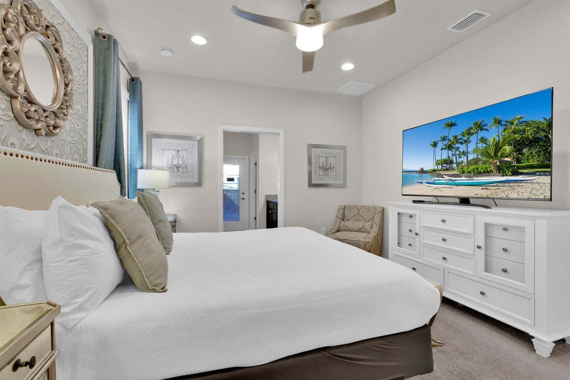 A bedroom with a bed, a TV, a ceiling fan, and a door leading to another room.