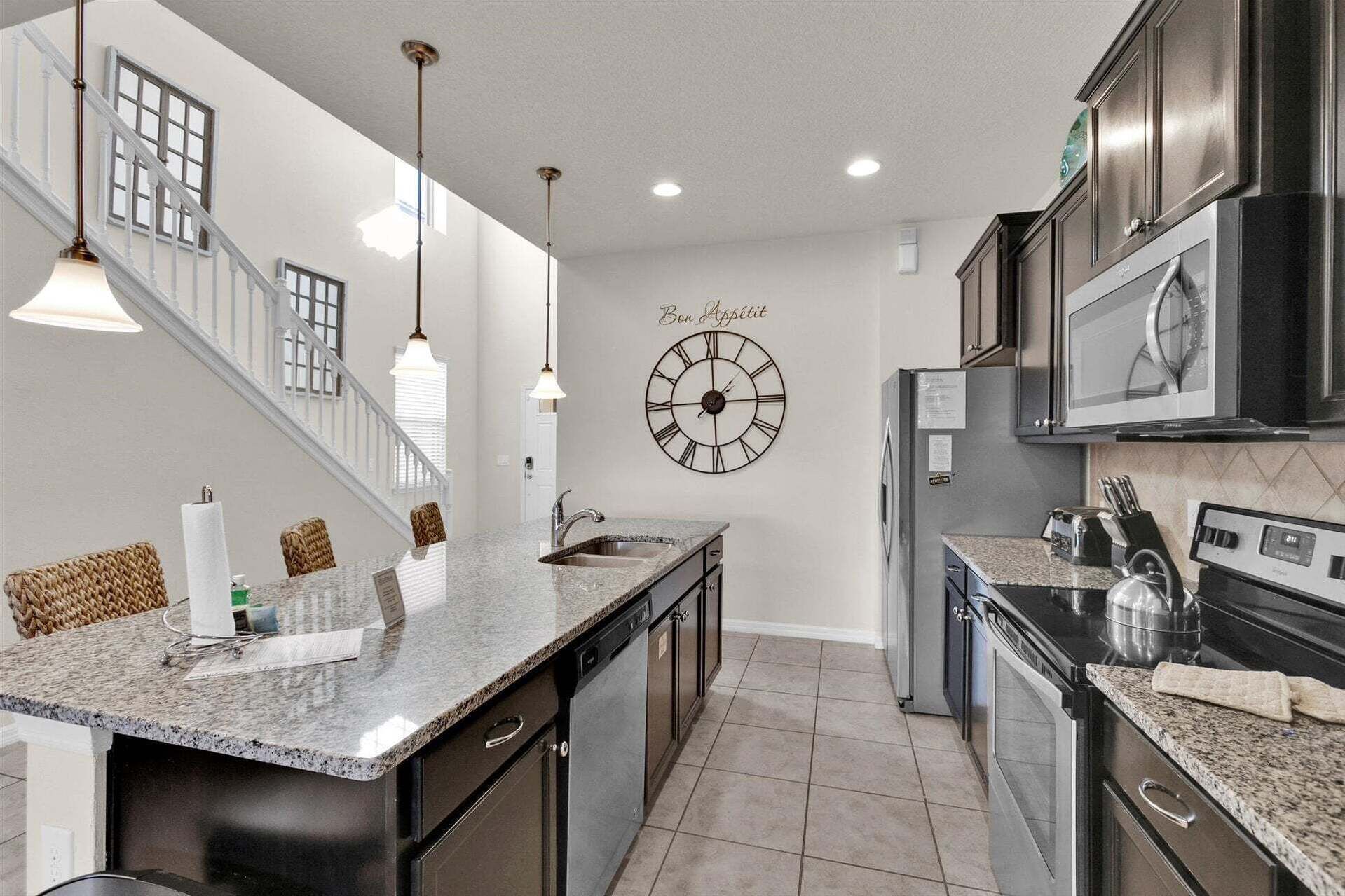 A modern kitchen with granite countertops, stainless steel appliances, and a clock on the wall.