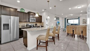 A modern kitchen with stainless steel appliances, a central island with chairs, and a dining area with a view. - Windsor Westside Resort 6 Bedroom Home With Game Room 0872 (Kissimmee)