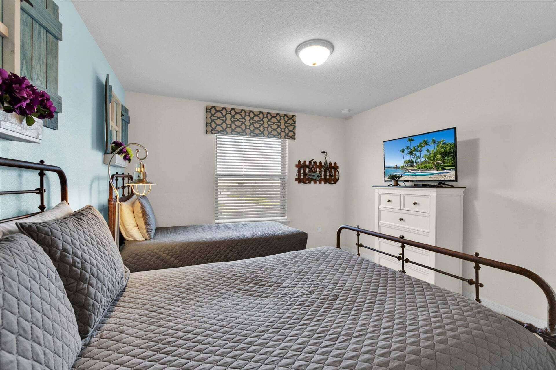 A bedroom with a bed, a dresser, a television, and a window with blinds.