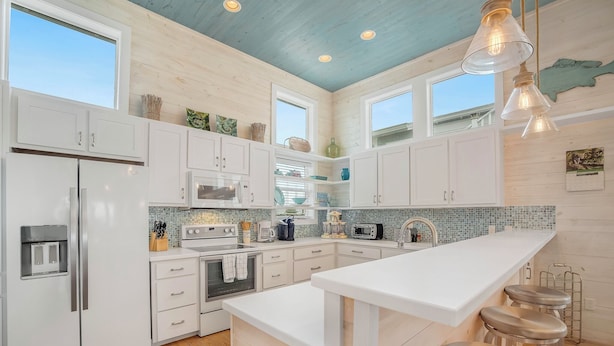 Una cucina moderna con mobili bianchi, un'isola grande con sgabelli e un soffitto blu.