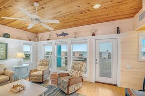 A cozy room with a ceiling fan, two wicker chairs, a small table, and a view through large windows. - Mermaid Retreat - Ocean Views! Golf Cart Included! (Port Aransas)