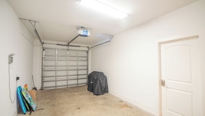 Un garage con una porta metallica chiusa, un proiettore a soffitto e una porta sulla destra.