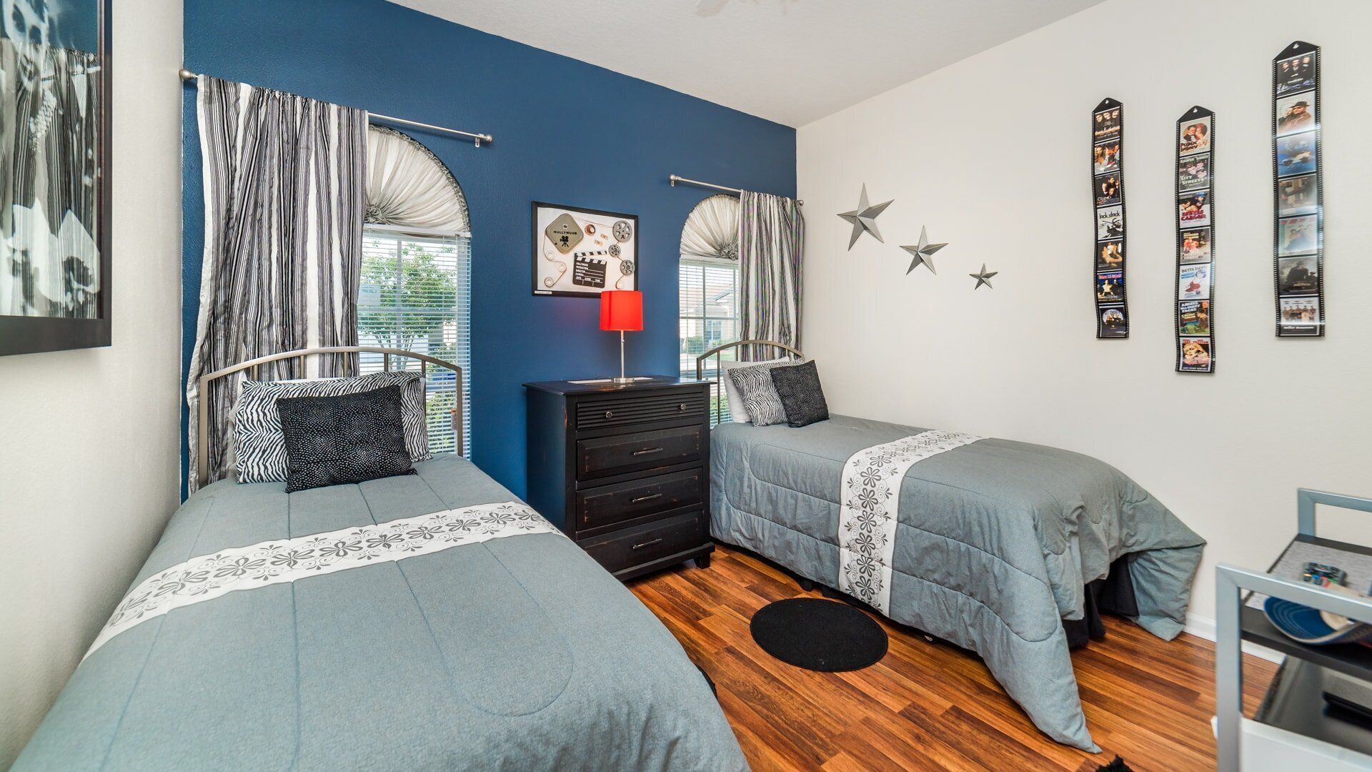 A bedroom with two single beds, a dresser, a red lamp, star decorations, and a wall with framed pictures.