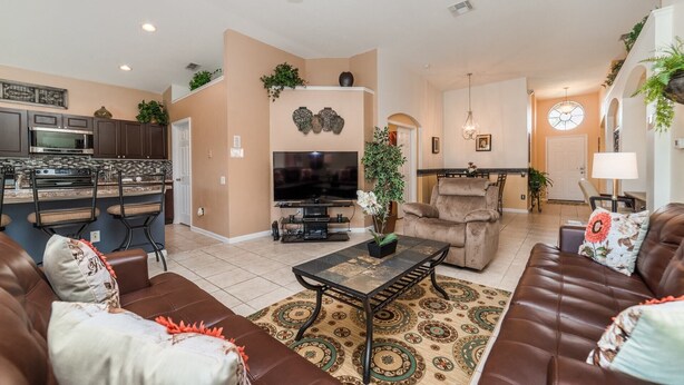 A spacious living room with a brown leather sofa, a TV, and a dining area with a kitchen in the background. - Windsor Palms Resort 4 Bedroom Home With Game Room 0843 (Kissimmee)