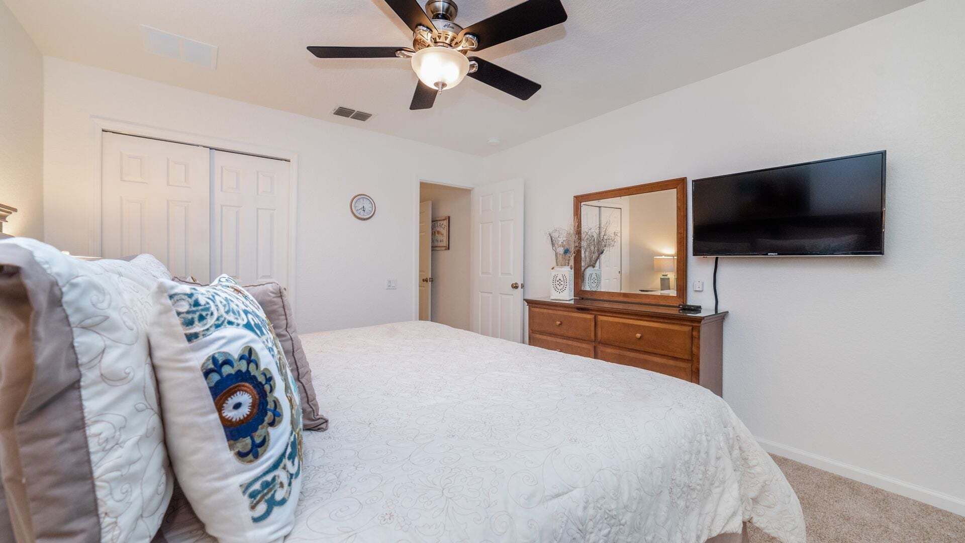 A bedroom with a bed, a dresser, a television, and a ceiling fan.
